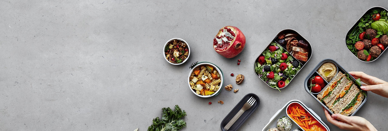 Reusable leak proof lunch boxes filled with healthy food on a grey bench