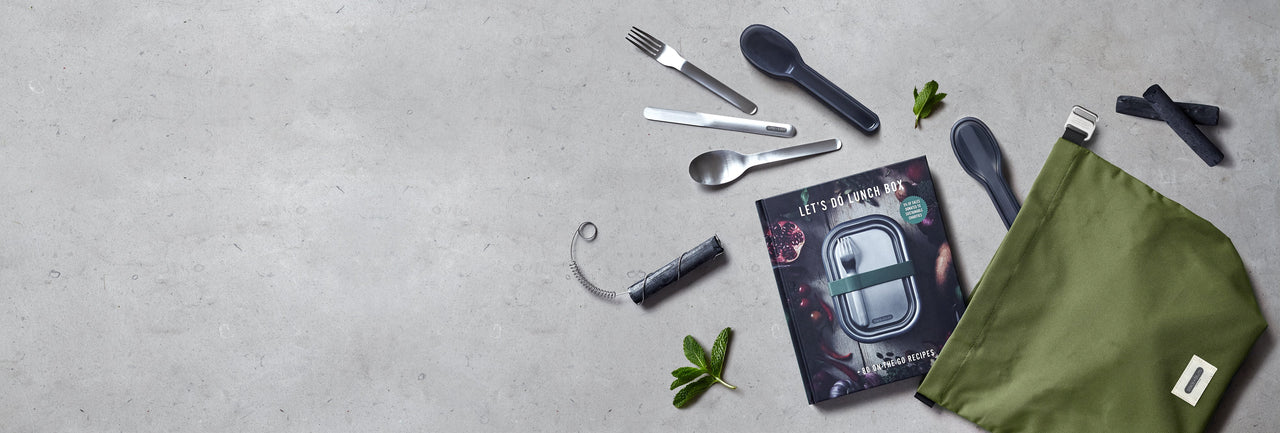 Sustainable lifestyle accessories including reusable cutlery set, active charcoal water filters and insulated leak proof lunch bag on grey bench